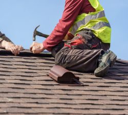 Two skilled Des Moines roof repair pros are installing asphalt shingles.