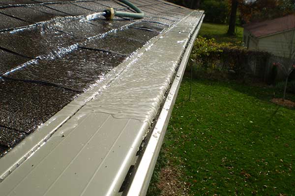 Light gray LeafX gutter guards taking in water from a hose on the roof